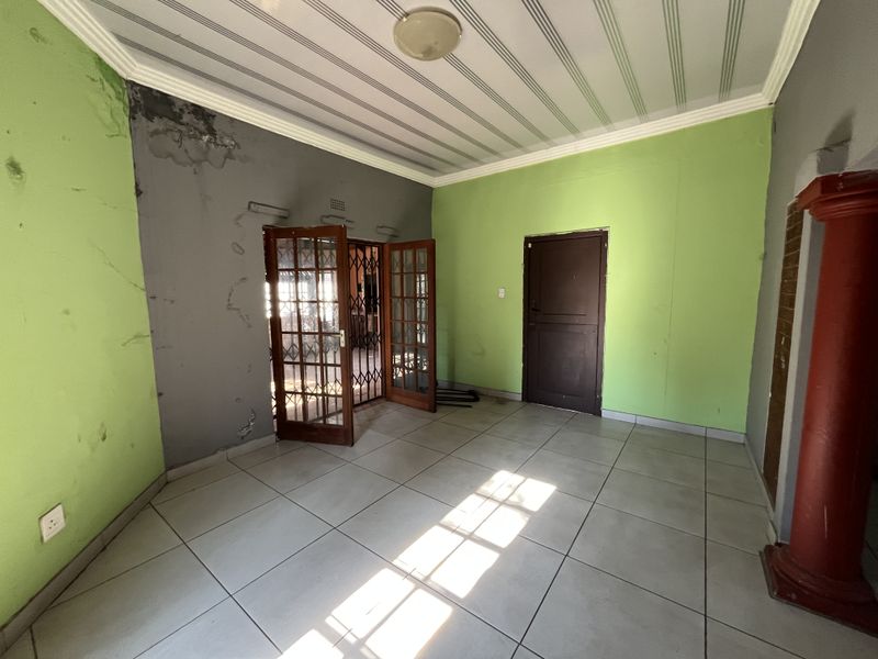 An empty living room featuring tiled flooring, french doors, and a decorative column, currently requiring wall repairs and cosmetic updates.