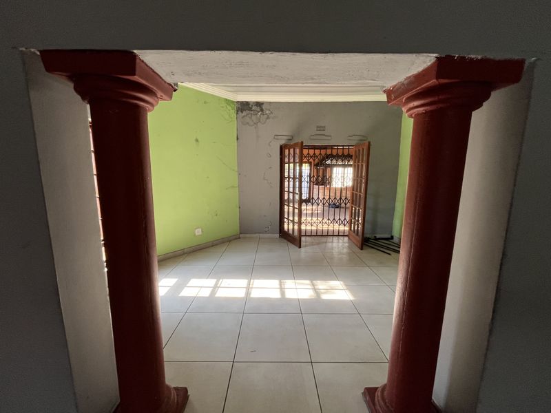 An empty living area featuring decorative columns, tiled flooring, and access to an outdoor space through security-gated french doors, requiring cosmetic wall repairs.