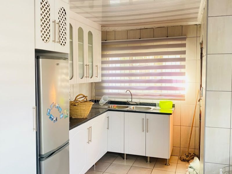 A functional kitchen featuring white built-in cabinetry, a double sink with mixer tap, tiled splashbacks, and tiled flooring.
