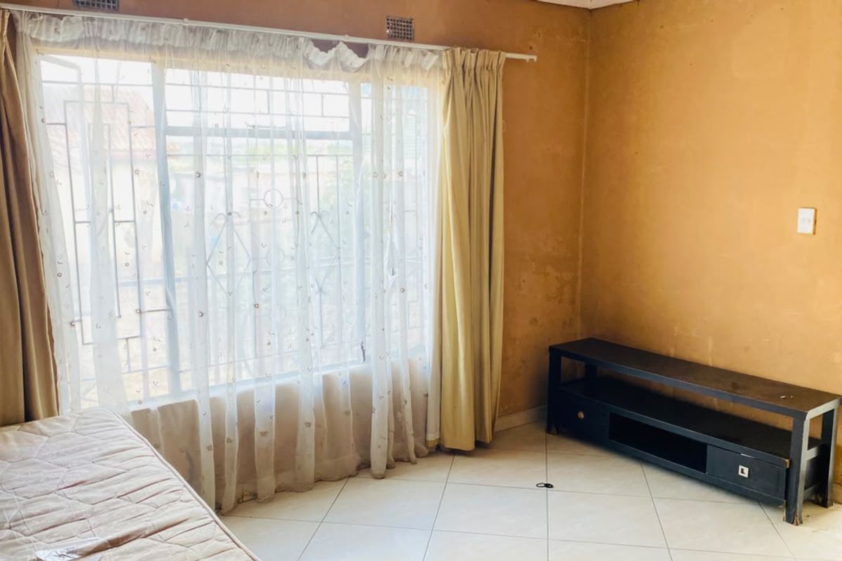 A bedroom featuring tiled flooring and a large window with security bars. The walls show signs of wear and require cosmetic attention.