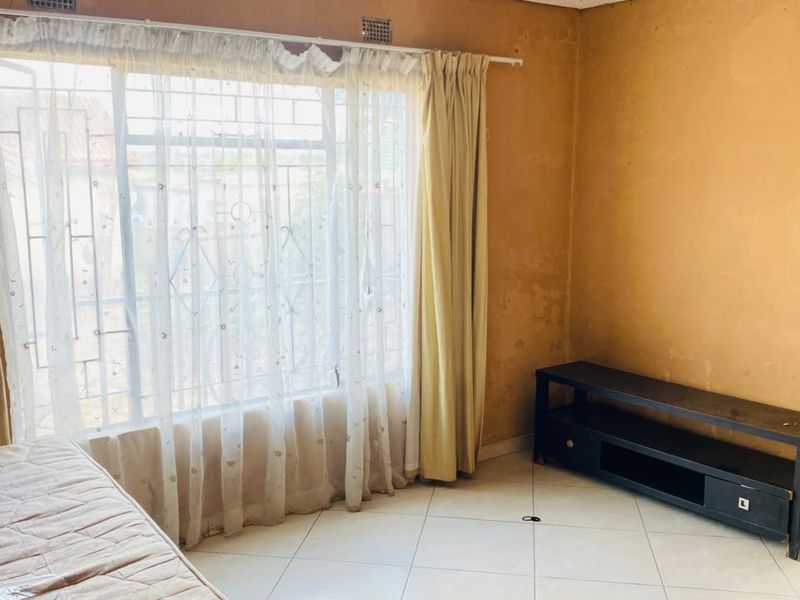 A bedroom featuring tiled flooring and a large window with security bars. The walls show signs of wear and require cosmetic attention.