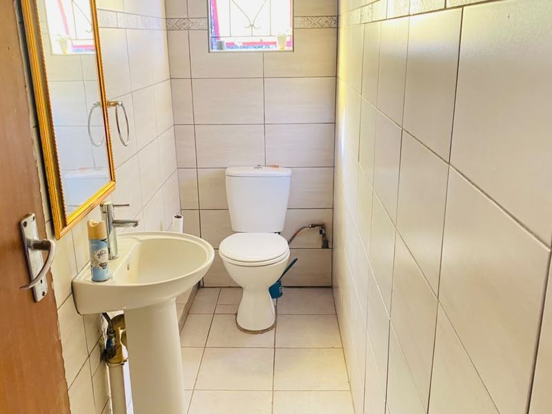 A compact bathroom featuring a pedestal basin, toilet, and neutral wall and floor tiling.