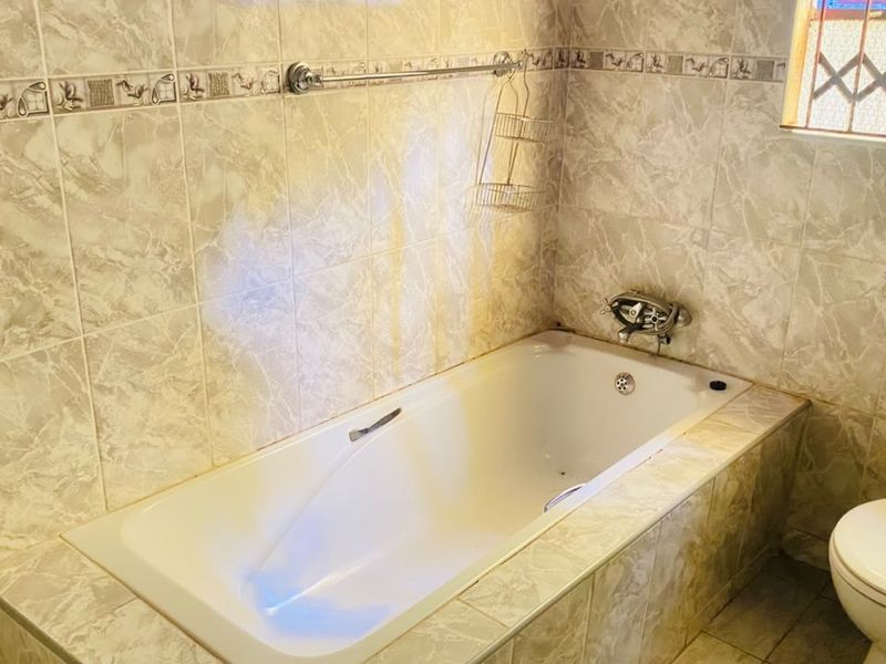 A functional bathroom featuring a built-in bathtub, ceramic wall tiling, and a standard toilet with a security grille on the window.