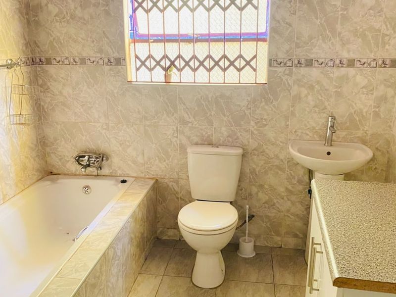 A functional bathroom featuring a bathtub, pedestal basin, and toilet, finished with neutral wall and floor tiles.