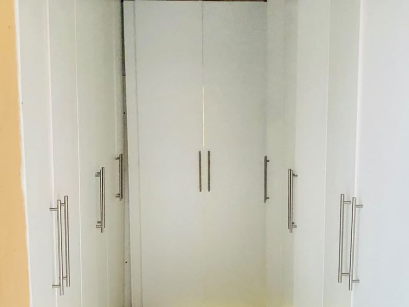 A narrow alcove featuring white built-in cupboards with stainless steel handles, showing signs of misalignment and wear.
