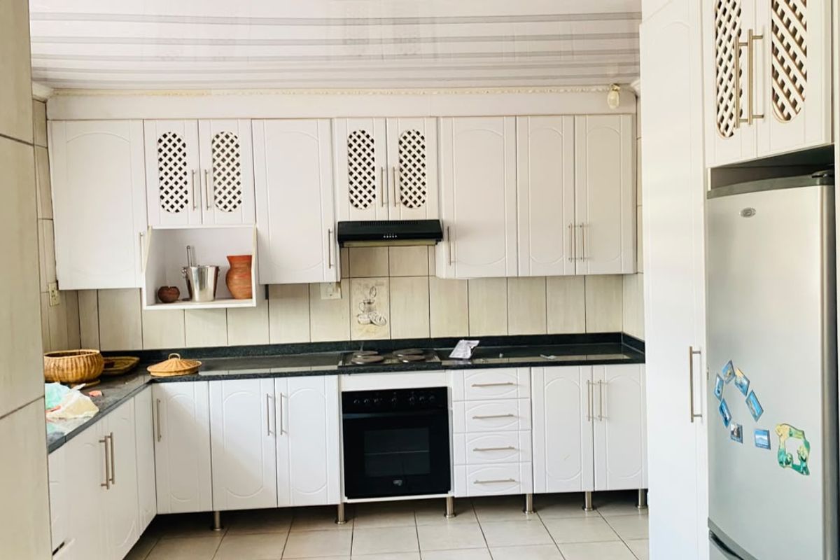 A functional kitchen featuring white cabinetry, a built-in oven with extractor fan, dark stone countertops, and tiled backsplash and flooring.