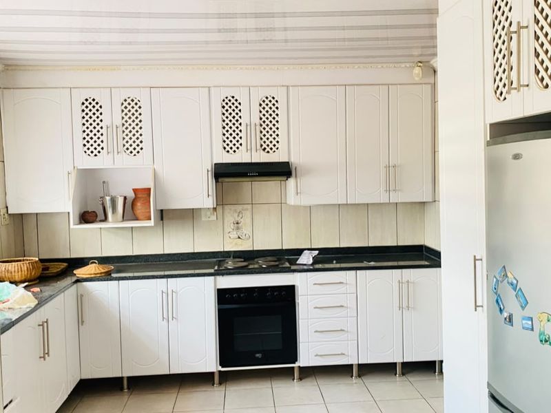 A functional kitchen featuring white cabinetry, a built-in oven with extractor fan, dark stone countertops, and tiled backsplash and flooring.