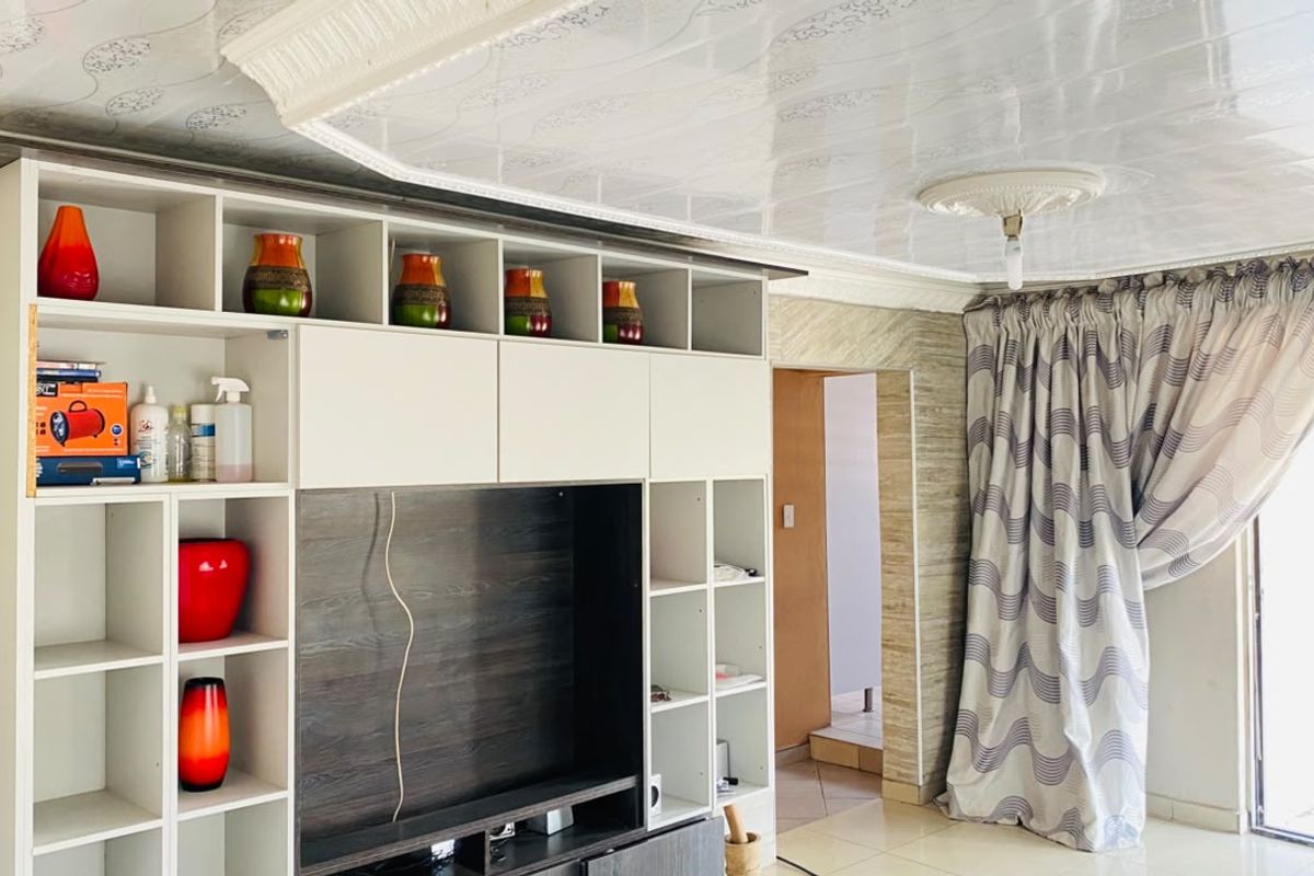 Living room featuring a large built-in media and storage unit, decorative ceiling panels with a central rose, and neutral tiled flooring.