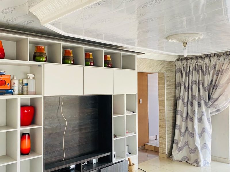 Living room featuring a large built-in media and storage unit, decorative ceiling panels with a central rose, and neutral tiled flooring.