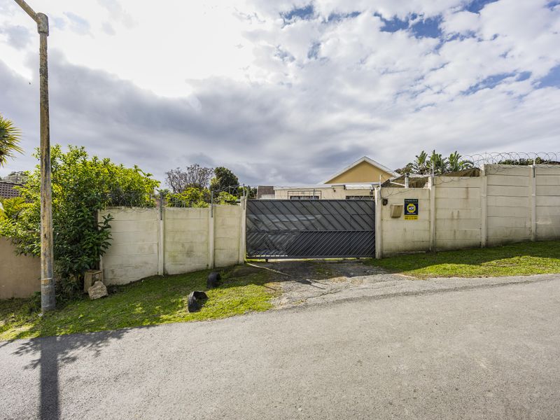 Front exterior view of the property featuring a precast concrete boundary wall with razor wire and a sliding metal driveway gate.