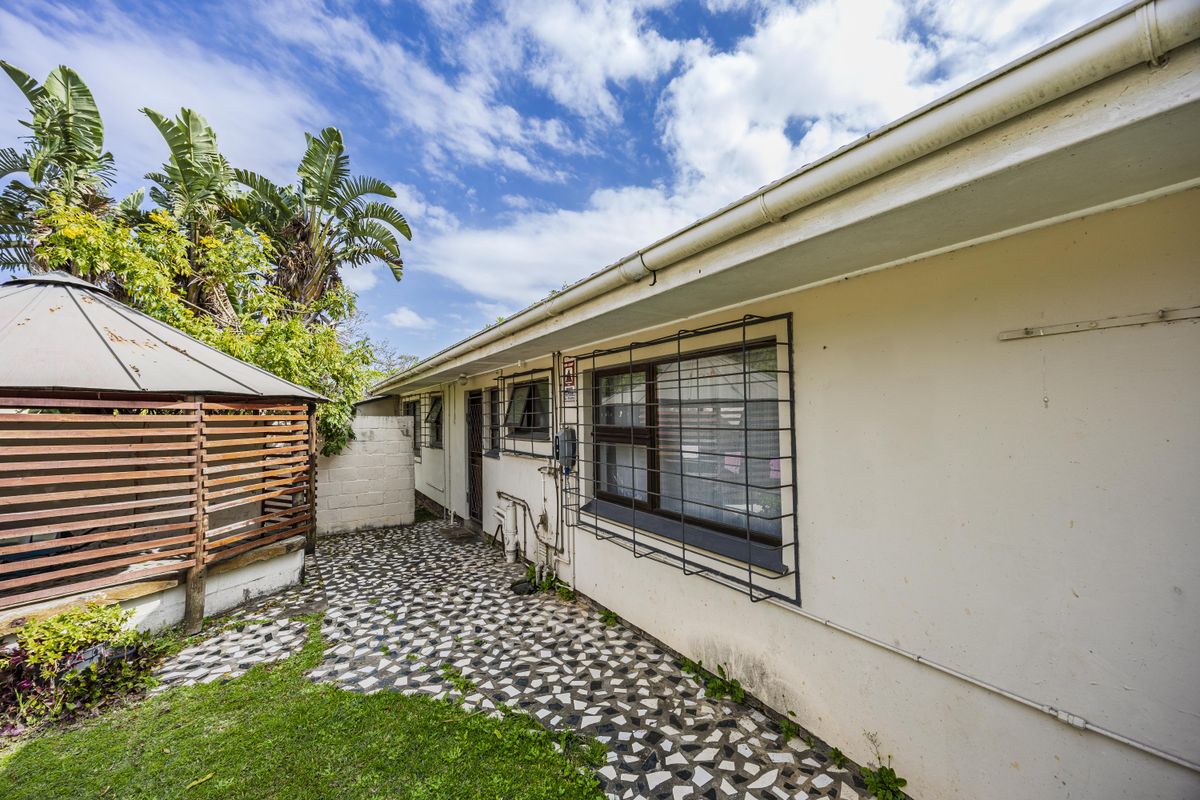 Rear exterior view of the property featuring a paved patio area, security bars on windows, and a detached gazebo structure.