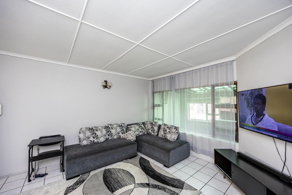 A living room featuring tiled flooring, a distinctive grid-pattern ceiling, and a large window providing natural light.
