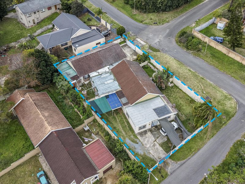 Aerial view of a residential property featuring a tiled roof house, concrete driveway, carport, and perimeter walling within a suburban neighborhood setting.
