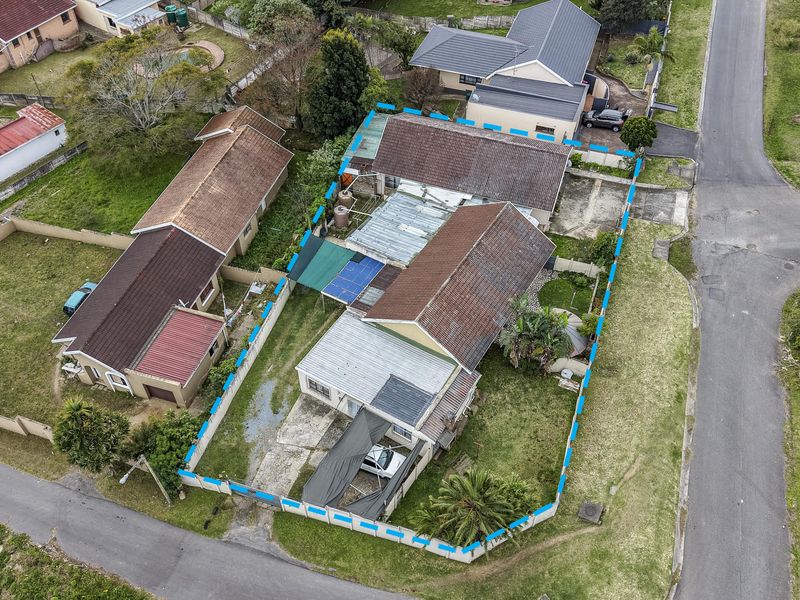 Aerial view of a residential property featuring a tiled roof, concrete driveway, carport, and surrounding garden area within a fenced perimeter.