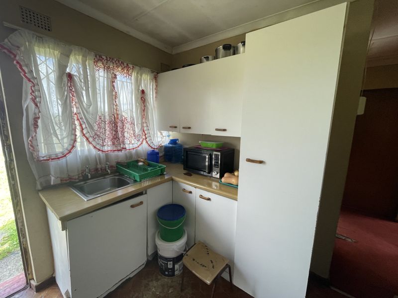 A compact kitchen featuring white built-in cabinetry, laminate countertops, and a stainless steel sink, offering potential for a modern renovation.