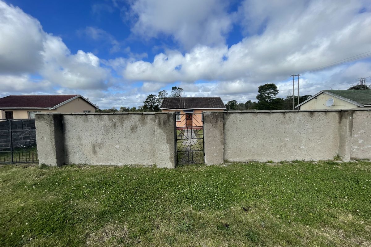 Front view of a detached house featuring a perimeter boundary wall, metal pedestrian gate, and a tiled roof structure.