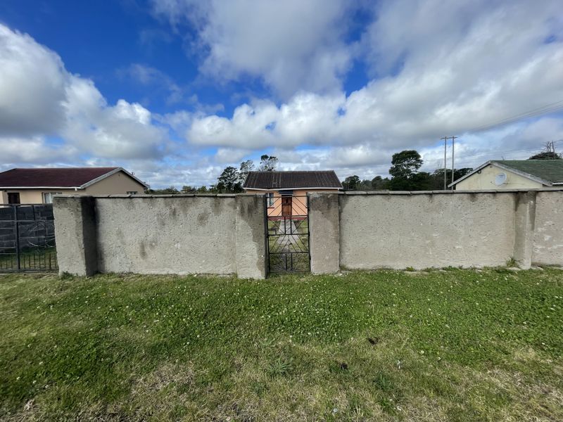 Front view of a detached house featuring a perimeter boundary wall, metal pedestrian gate, and a tiled roof structure.