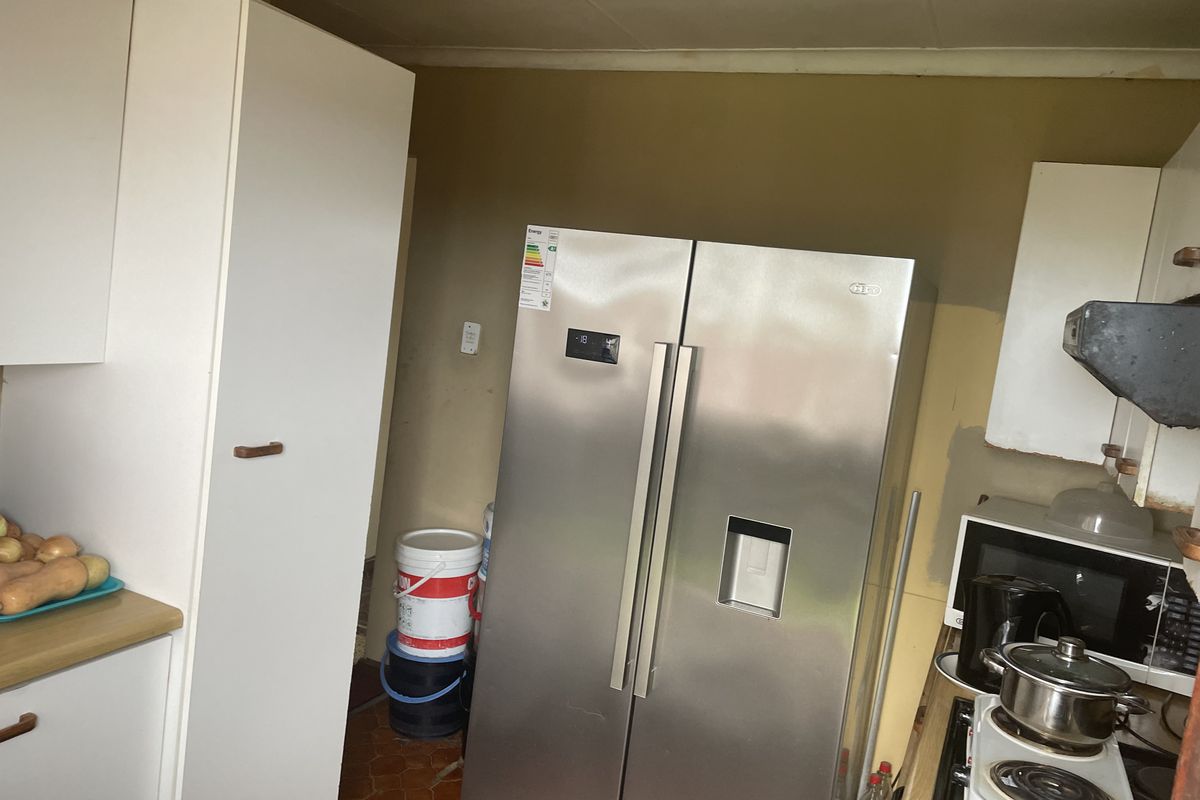 A dated kitchen area featuring white cabinetry, laminate countertops, and a built-in hob with extractor fan, requiring cosmetic updates to improve the overall aesthetic.