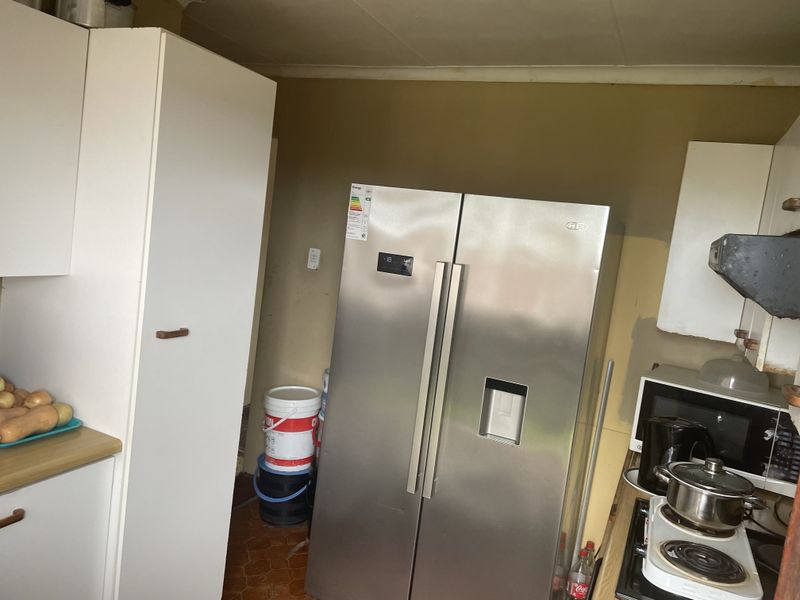 A dated kitchen area featuring white cabinetry, laminate countertops, and a built-in hob with extractor fan, requiring cosmetic updates to improve the overall aesthetic.