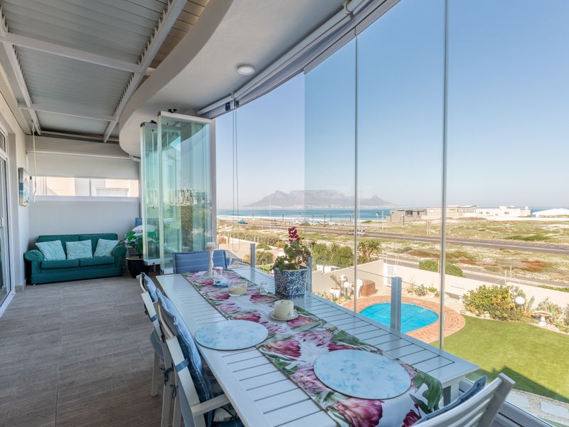 A spacious covered balcony featuring glass stackable doors, tiled flooring, and panoramic views of the coastline and Table Mountain.
