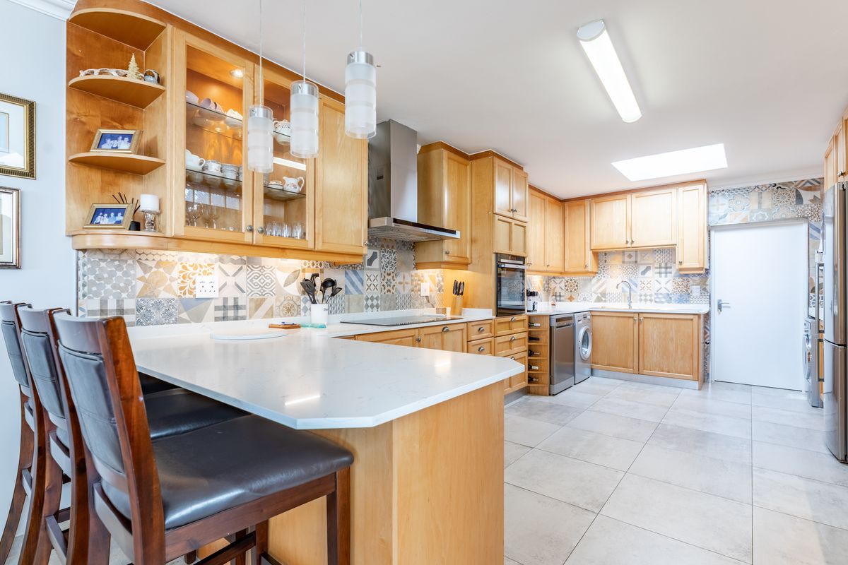 Spacious kitchen featuring light wood cabinetry, stone countertops, a decorative tiled backsplash, integrated appliances, and a skylight for natural illumination.