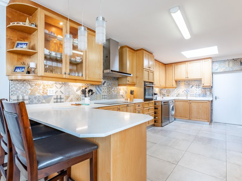 Spacious kitchen featuring light wood cabinetry, stone countertops, a decorative tiled backsplash, integrated appliances, and a skylight for natural illumination.
