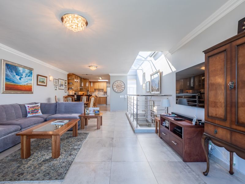 Spacious open-plan living area featuring tiled floors, a modern staircase with metal balustrades, a skylight, and an integrated kitchen space.