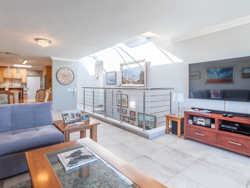 Spacious open-plan living and kitchen area featuring tiled floors, a modern stainless steel balustrade, and a large skylight providing ample natural light.