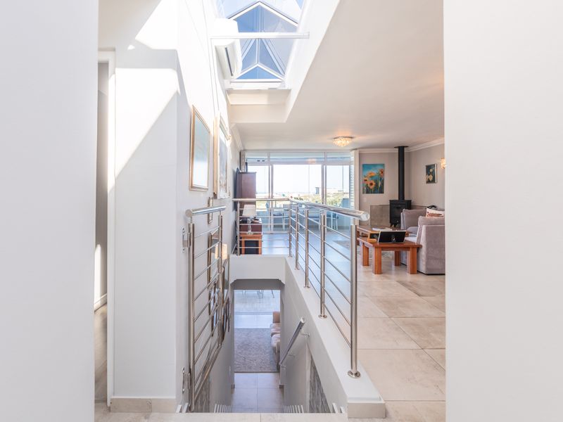 Bright, open-plan hallway featuring a large skylight, modern stainless steel balustrades, and tiled flooring, leading into a spacious living area with a fireplace.