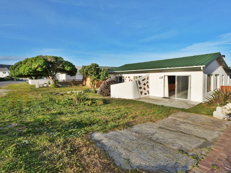 Front exterior view of a single-story house featuring a green metal roof, sliding glass doors, and a concrete driveway set on a grassy plot.