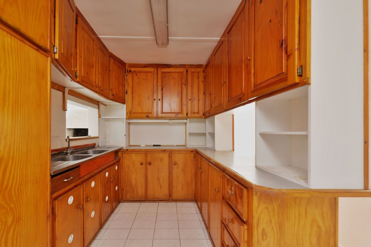 A dated kitchen featuring extensive wooden cabinetry, a double bowl stainless steel sink, and tiled flooring, offering significant potential for a modern renovation.