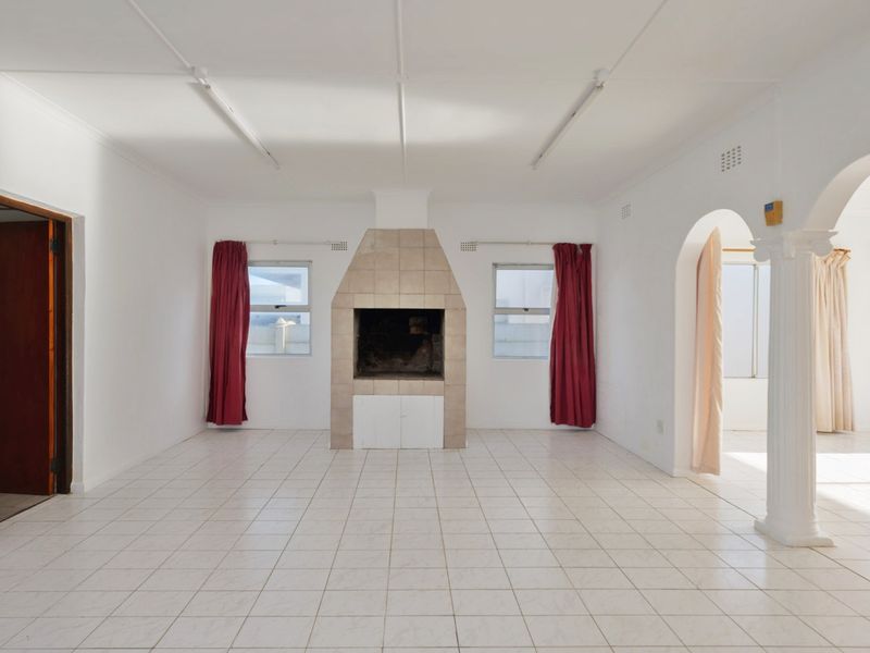 Spacious living room featuring tiled flooring, a central built-in fireplace, and an elegant archway with a decorative column.