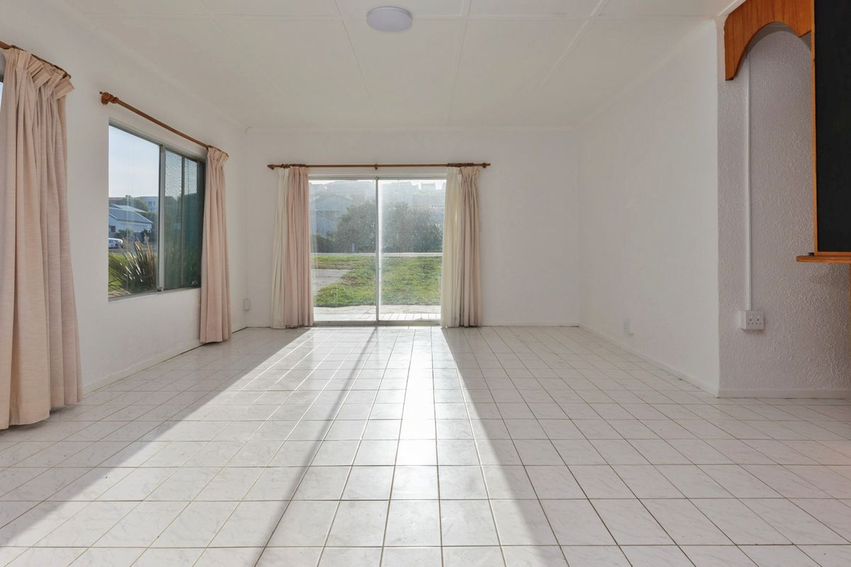 A bright, empty living room featuring white tiled flooring, a built-in bar counter, and sliding glass doors leading to the exterior.
