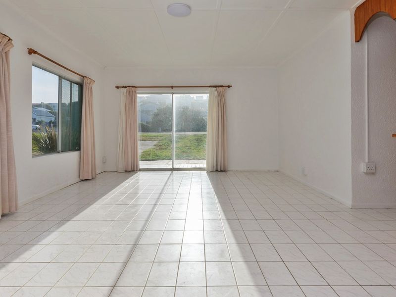 A bright, empty living room featuring white tiled flooring, a built-in bar counter, and sliding glass doors leading to the exterior.