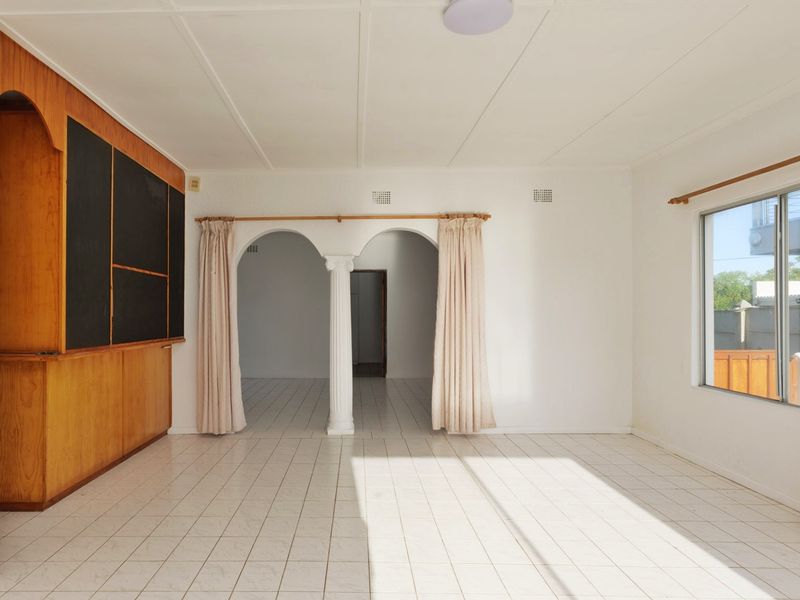 Spacious living area featuring a built-in wooden bar, arched architectural details, and tiled flooring, offering a versatile blank canvas for renovation.
