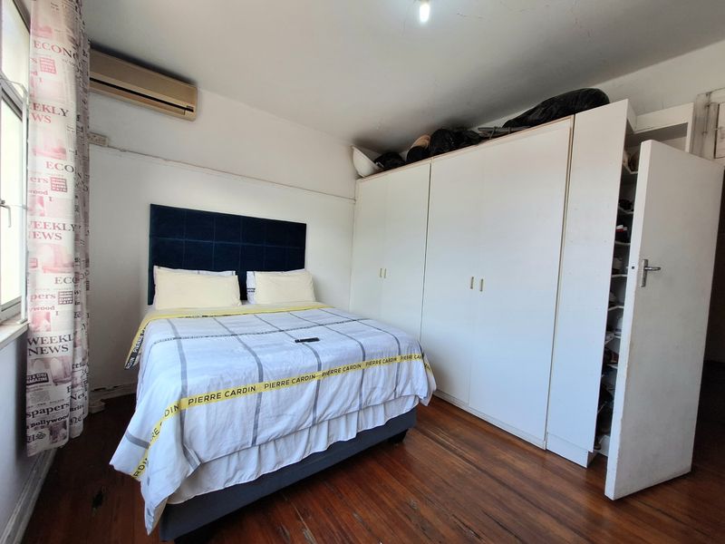 A bedroom featuring timber flooring, built-in cupboards, and an air conditioning unit.