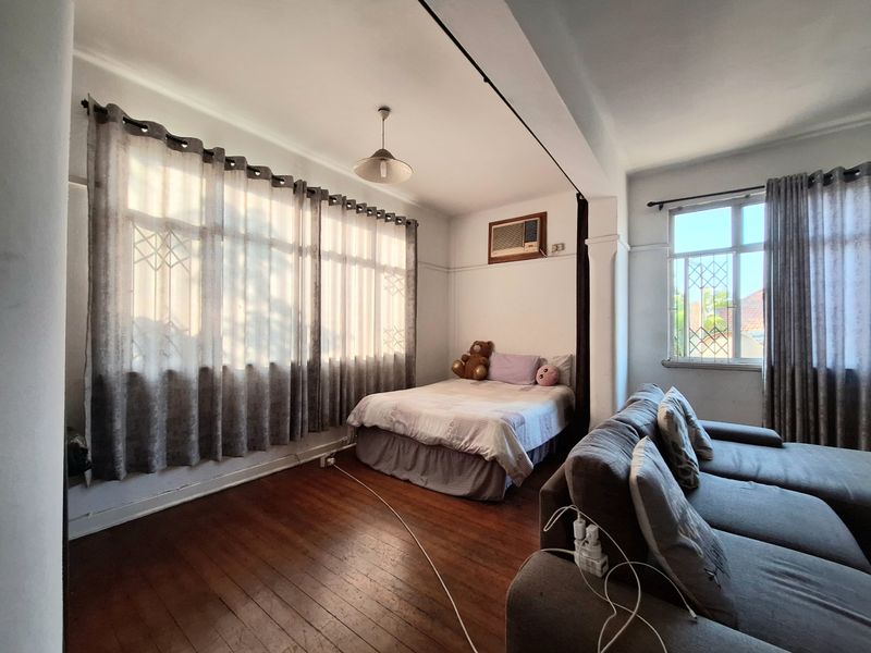Open-plan living and sleeping area featuring hardwood flooring, large windows with security bars, and a wall-mounted air conditioning unit.