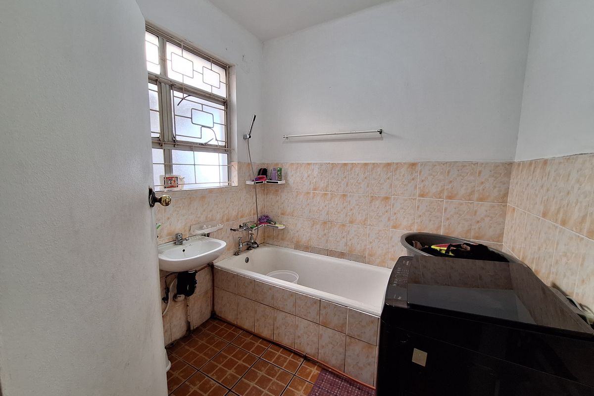 A functional bathroom featuring a bathtub with shower mixer, pedestal basin, and tiled finishes, requiring cosmetic updates to modernize the space.