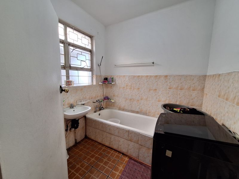 A functional bathroom featuring a bathtub with shower mixer, pedestal basin, and tiled finishes, requiring cosmetic updates to modernize the space.
