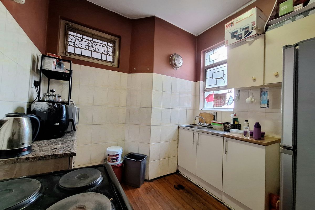 A functional kitchen featuring built-in cabinetry, a stainless steel sink, tiled splashbacks, and hardwood flooring, with security bars installed on the windows.