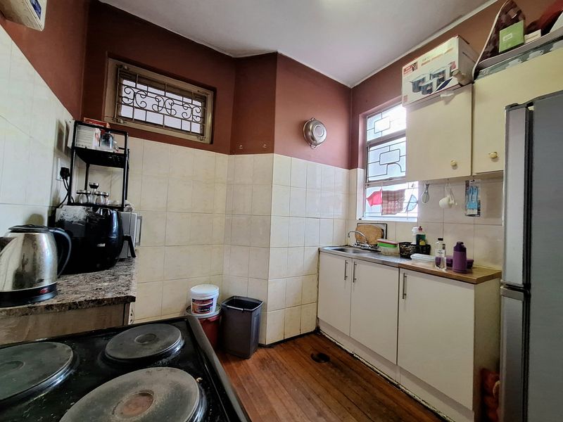 A functional kitchen featuring built-in cabinetry, a stainless steel sink, tiled splashbacks, and hardwood flooring, with security bars installed on the windows.