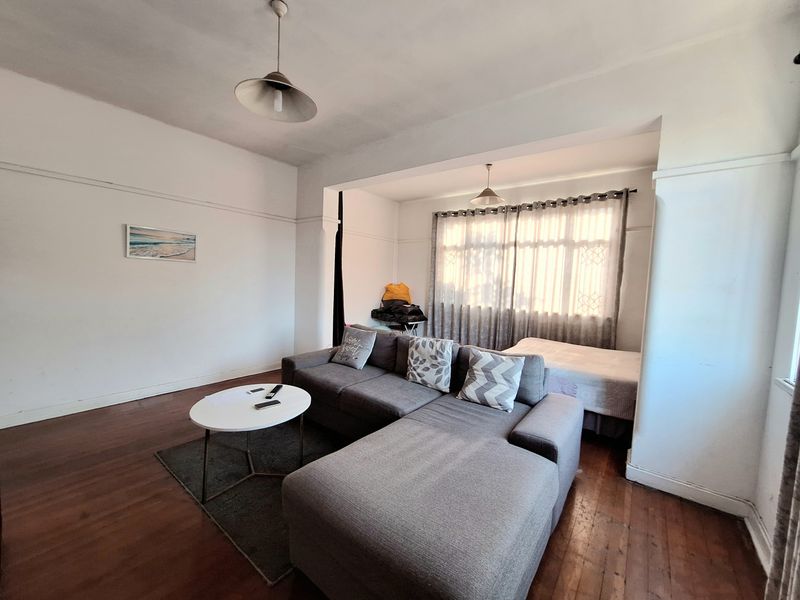 A living room featuring original hardwood flooring, picture rails, and neutral wall finishes, offering a functional space with potential for modern updates.