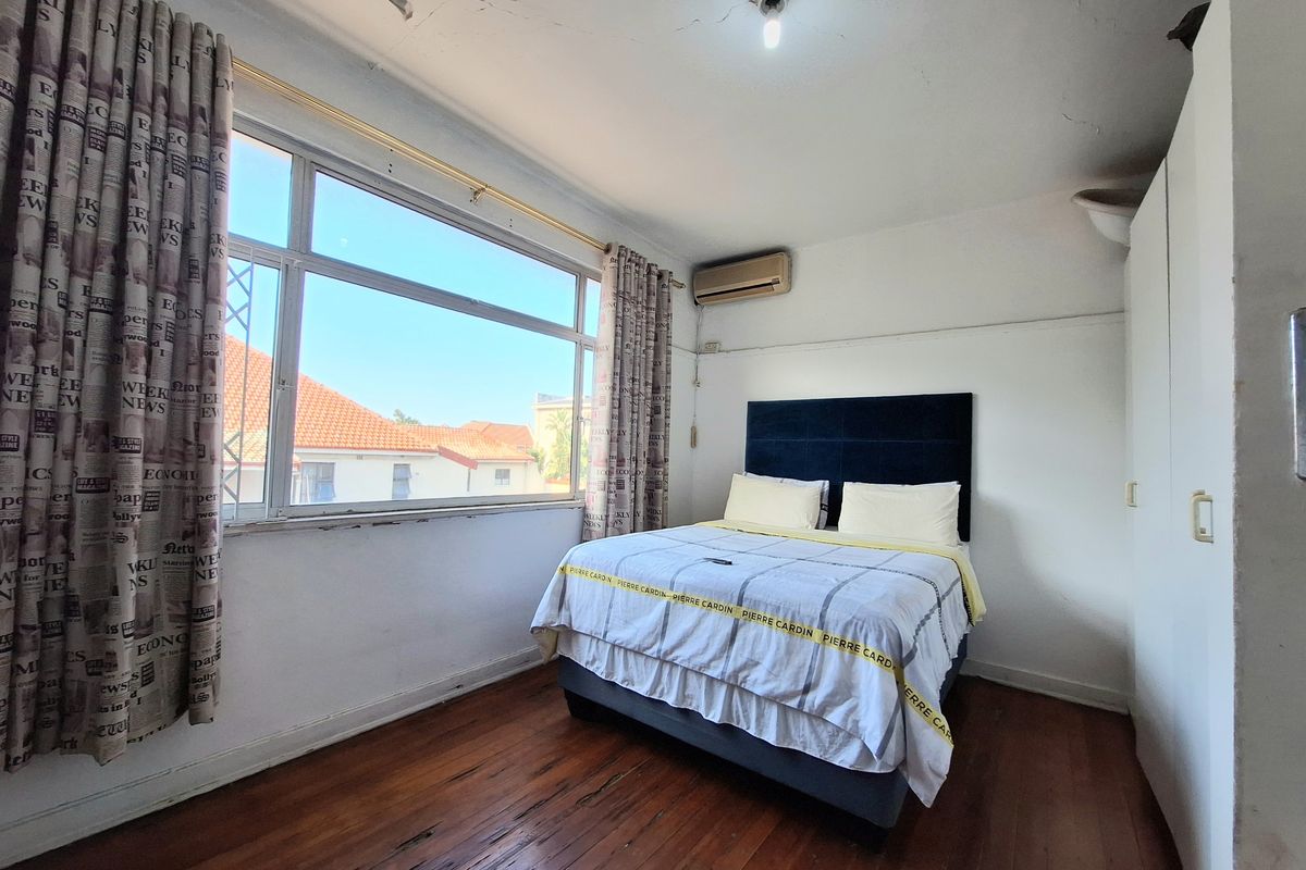 A bedroom featuring timber flooring, built-in wardrobe, and an air conditioning unit, with visible signs of wear on the ceiling and floor.