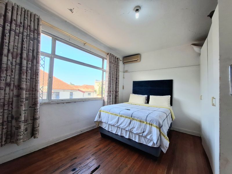 A bedroom featuring timber flooring, built-in wardrobe, and an air conditioning unit, with visible signs of wear on the ceiling and floor.