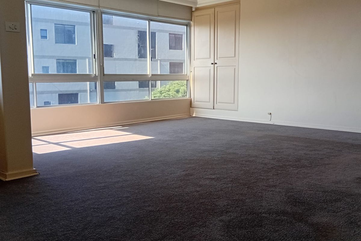 Spacious bedroom featuring neutral walls, built-in wardrobe storage, crown molding, and large windows providing natural light.