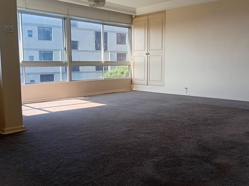 Spacious bedroom featuring neutral walls, built-in wardrobe storage, crown molding, and large windows providing natural light.