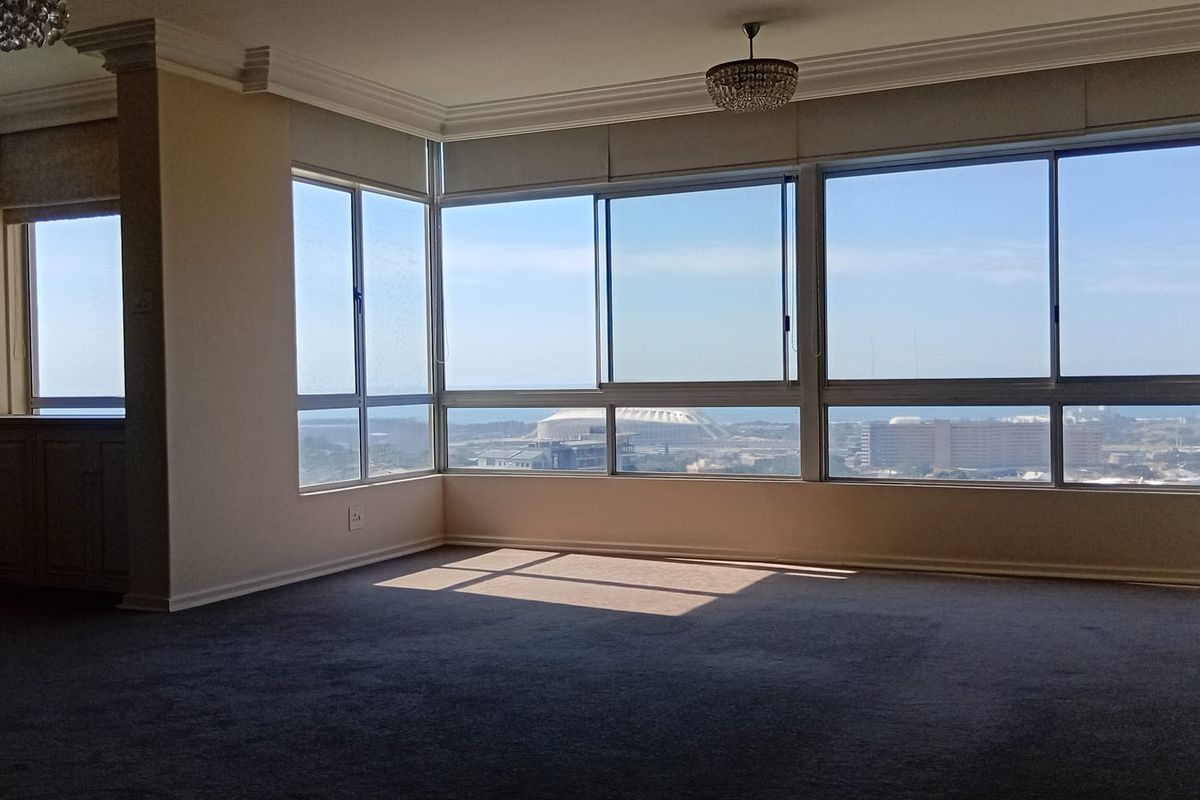 Spacious living area featuring expansive windows with panoramic city and coastal views, crown molding, and neutral carpeting.