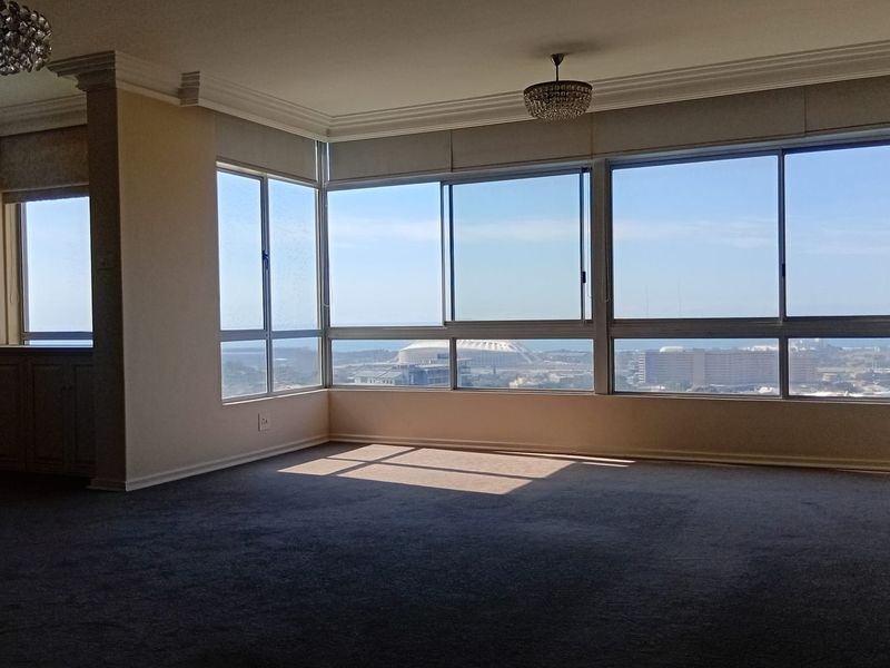 Spacious living area featuring expansive windows with panoramic city and coastal views, crown molding, and neutral carpeting.