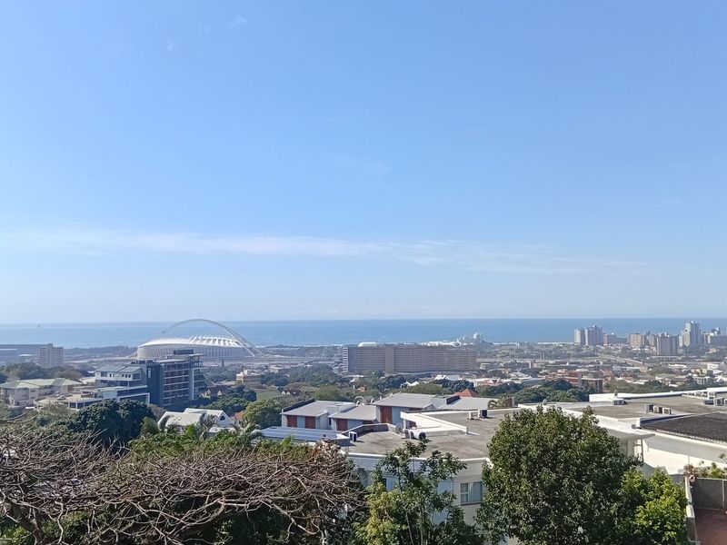 An elevated panoramic view overlooking the cityscape, stadium, and coastline under a clear blue sky.