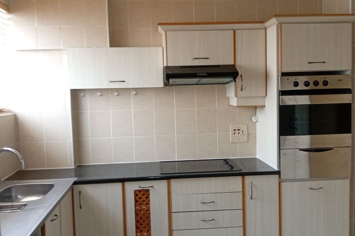 A functional kitchen featuring built-in cabinetry, a stainless steel sink, integrated oven, electric hob, and extractor fan with neutral tiled finishes.